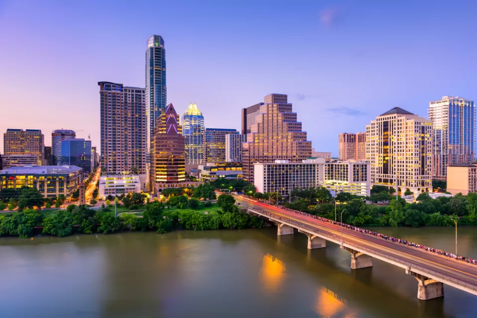 View of Austin, Texas skyline at dusk with Colorado River and bridge in foreground